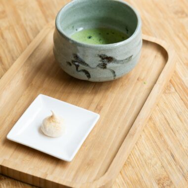 Ceramic cup of matcha green tea with dessert on a wooden tray, minimalistic setting.