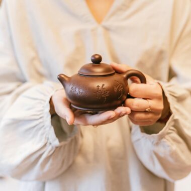 Close-up of a person holding a decorative ceramic teapot in a serene setting.