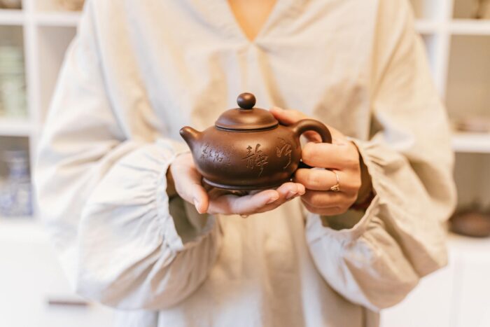 Close-up of a person holding a decorative ceramic teapot in a serene setting.