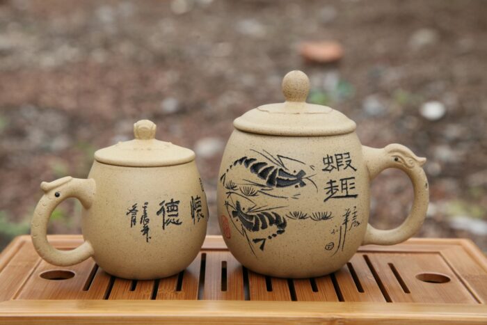 Pair of traditional Japanese clay teapots with painted designs on a wooden tray.