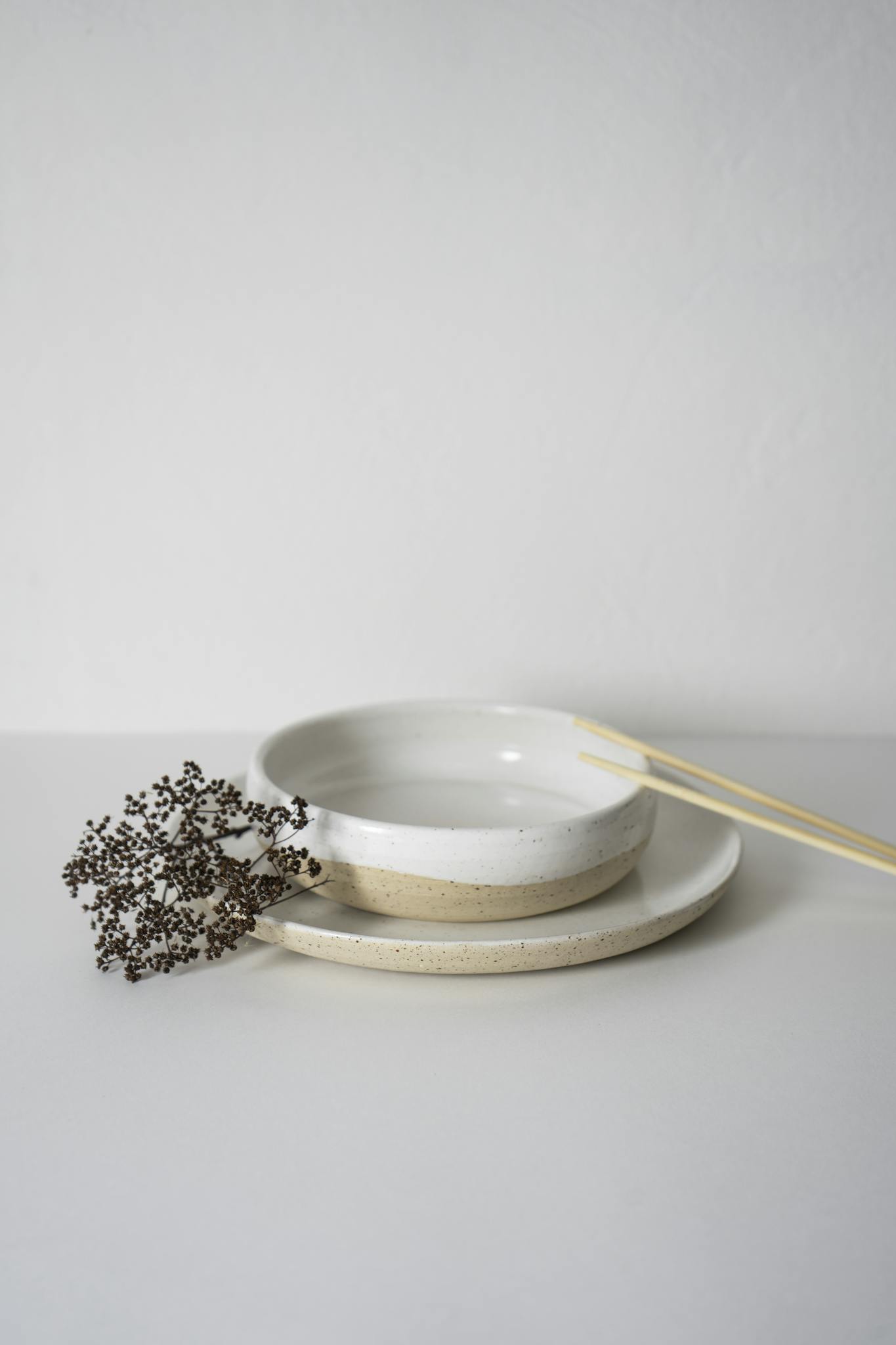 Simple and elegant white ceramic bowls with chopsticks on a plain background.