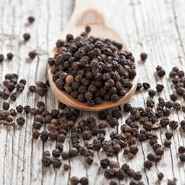 wooden spoon with peppercorns on rustic foreground and background