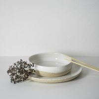 Simple and elegant white ceramic bowls with chopsticks on a plain background.
