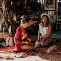 Two women crafting souvenirs in a vibrant Thai shop, surrounded by art and textiles.